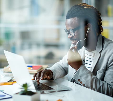 Young black man sitting at his desk and working on laptop while making a phone call