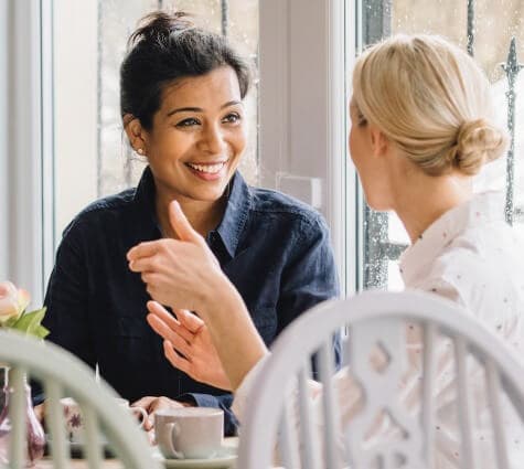 White woman and Asian woman sitting at a table and engaging in word of mouth marketing