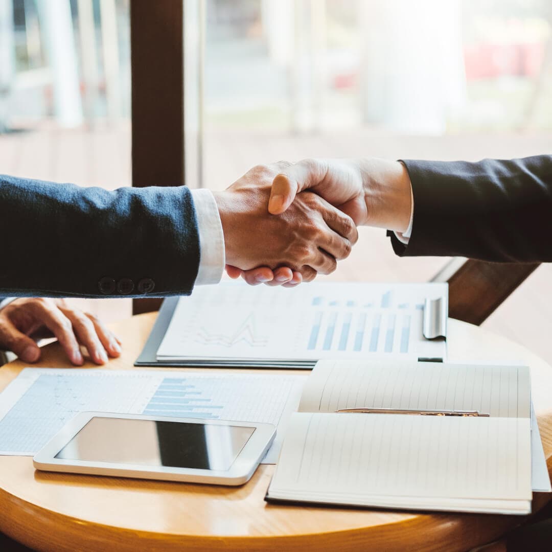 People shaking hands over a stack of financial paperwork