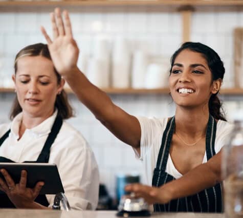 Young South Asian business owner standing at the counter of coffee shop and ringing a bell