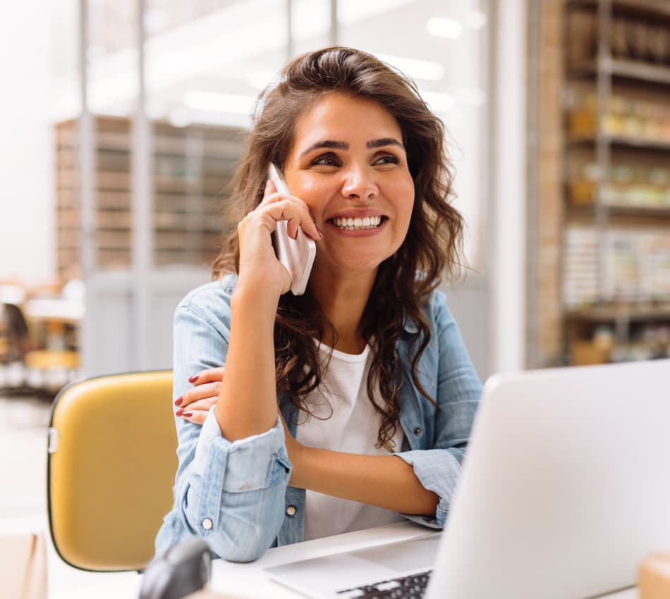 Woman sitting in an office on a phone call, with a laptop in front of her.