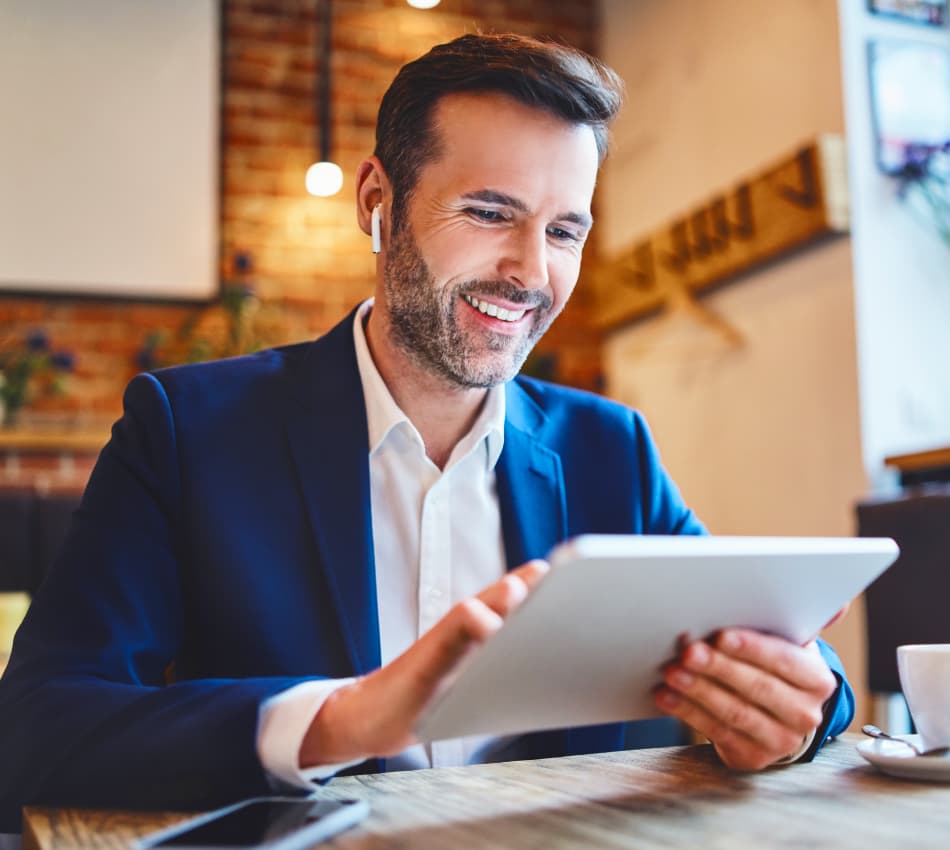 Man in suit smiling while sitting in cafe using a tablet.