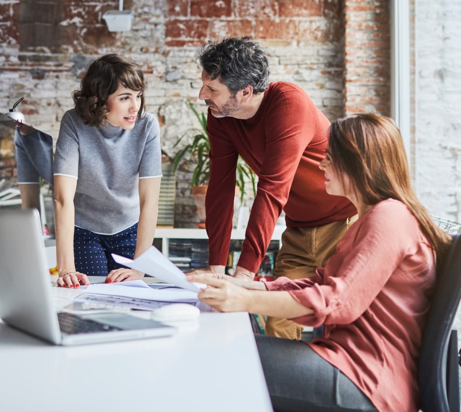 Three small business employees gather around a desk to discuss business plans.