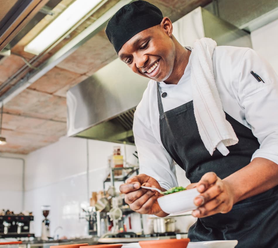 Chef in kitchen spoons chimichurri into bowls.