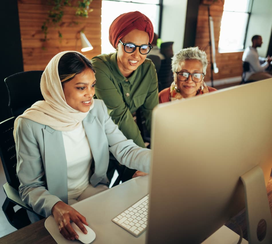 Three women looking on at a large computer screen.