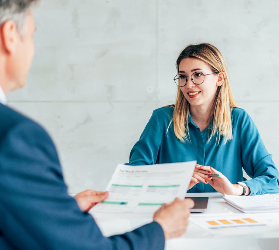 Investor reviews sheet with numbers while woman business owner makes her pitch.
