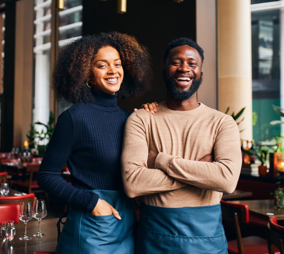 Two married business owners smile in their restaurant.