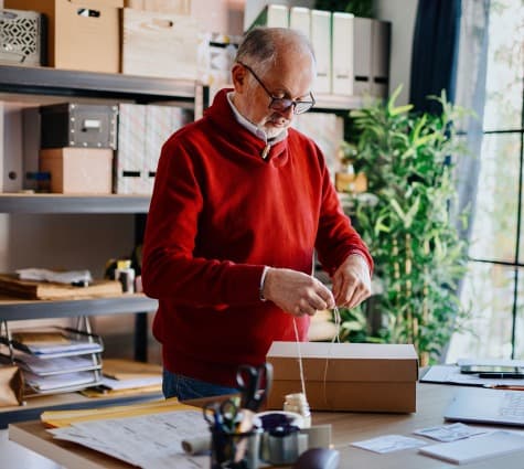Older gentleman in red sweater tying ribbon around a wrapped package for the holidays