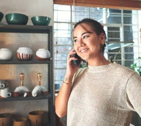 Smiling young Asian woman on the phone in her pottery shop and studio.