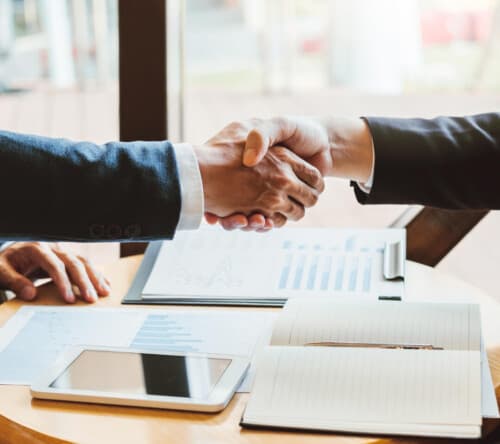 People shaking hands over a stack of financial paperwork