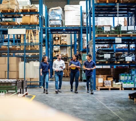 Crew of warehouse workers and business owner walking in warehouse and talking.