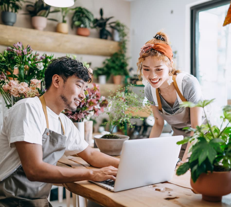Man and woman smile at laptop screen in florist shop.