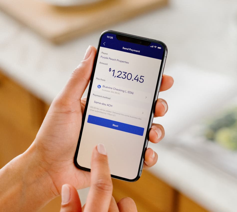 Close-up of hands holding a phone while the person sends a same-day ACH payment from their Bluevine Business Checking account.