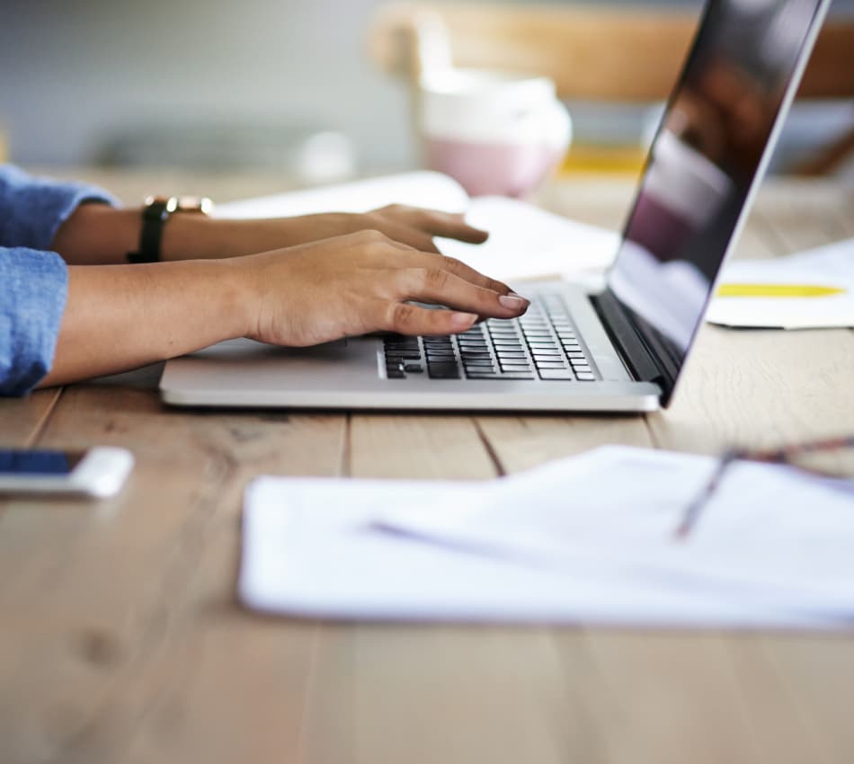 Close-up of hands with sleeves rolled up typing on a laptop.