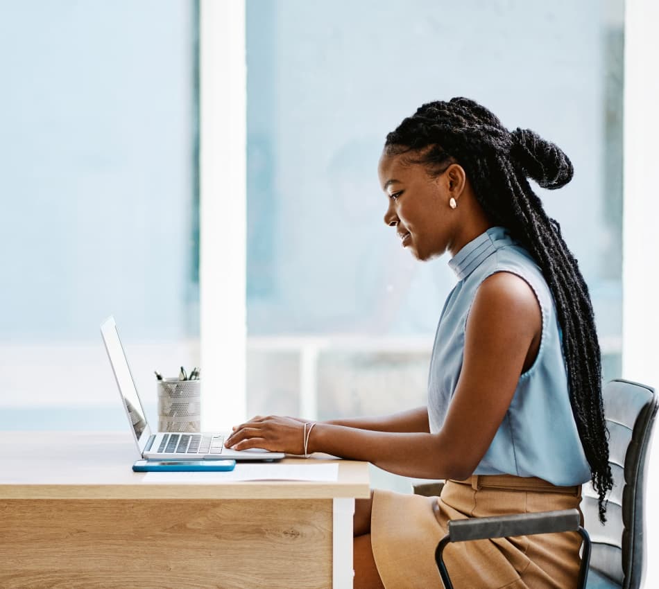 Young woman sitting at a desk with a laptop, her phone, and papers.