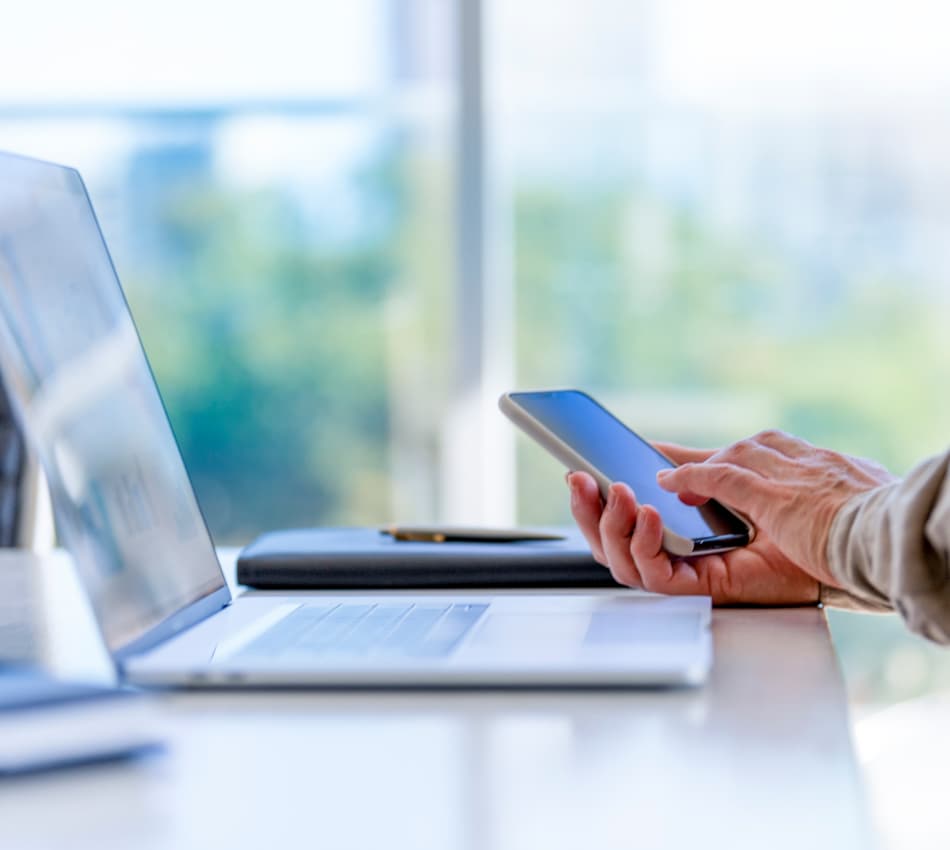 Close up of hands holding a phone near a laptop.