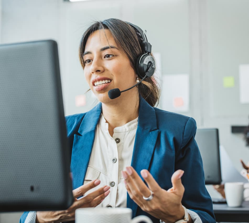 Female sales rep wears a headset and speaks to prospect on the phone while looking at her computer screen.