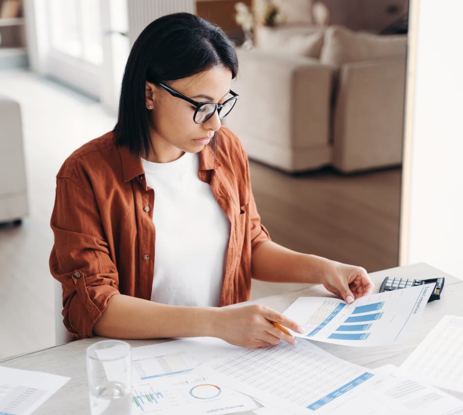 Woman looks through graphs and charts with calculator next to her.