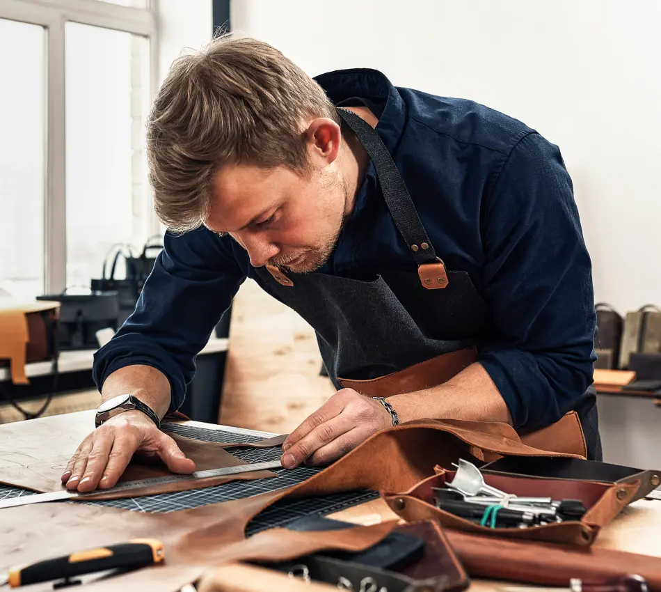 Small business owner focuses on precisely measuring and cutting a piece of leather.