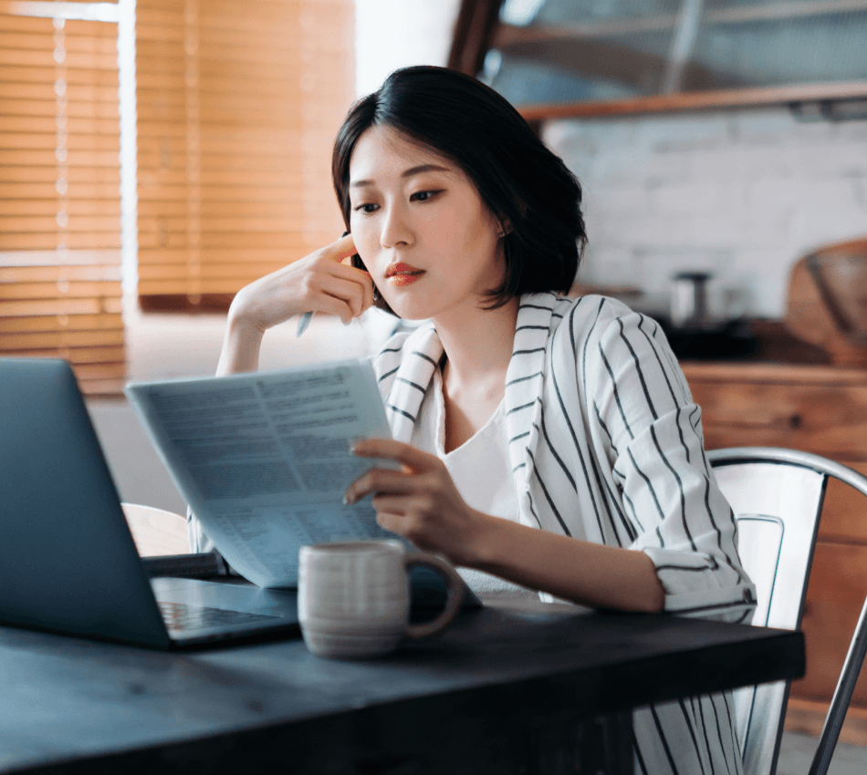 Female business owner reads over tax return documents in front of her laptop.