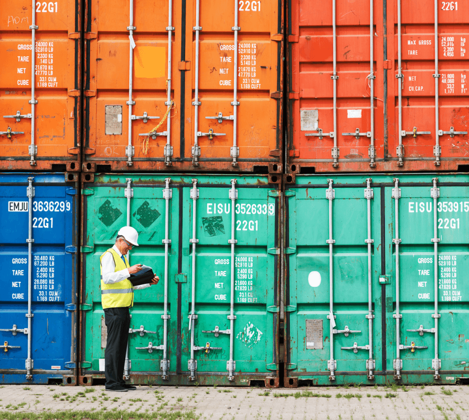 Man in hard hat checks log while reviewing shipping containers.