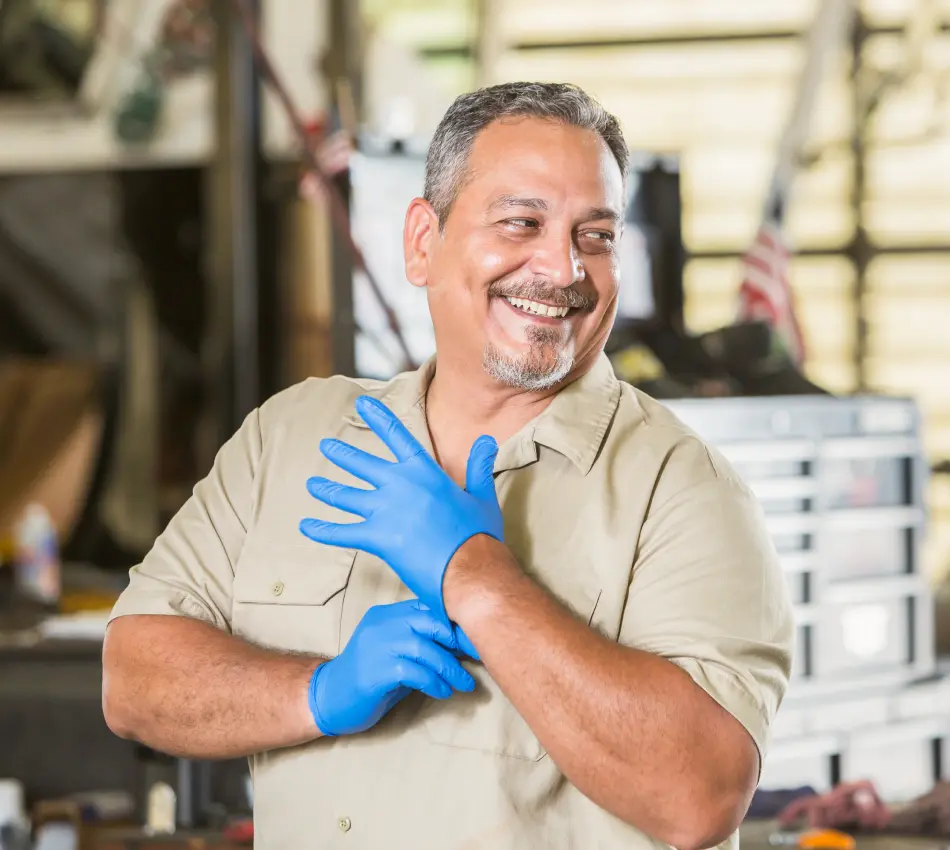Male business owner puts on gloves to work in auto repair shop.